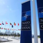 NATO flags and banners under clear sky.