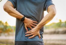 Person holding lower back in discomfort outdoors