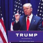 Deep State PANICS as Trump Reshapes NSC Man speaking at podium with USA flags behind him