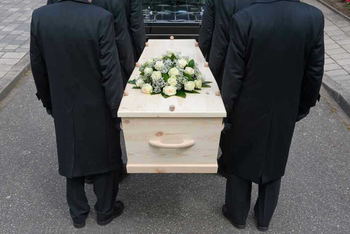 144558722 Four people carrying a coffin with white flowers