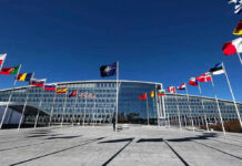 Flags outside NATO headquarters building under clear blue sky