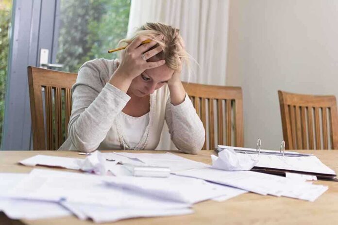 A woman sitting at a desk with her head in her hands surrounded by paperwork
