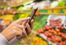 Person using a smartphone while shopping for fresh produce in a grocery store