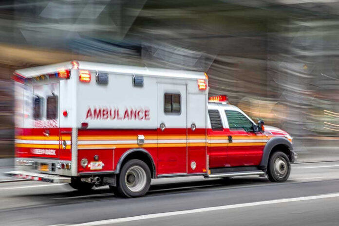 1495131698 Red and white ambulance driving on street.