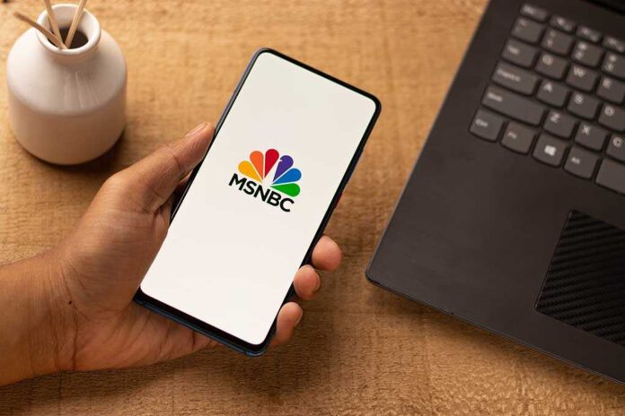A hand holding a smartphone displaying the MSNBC logo