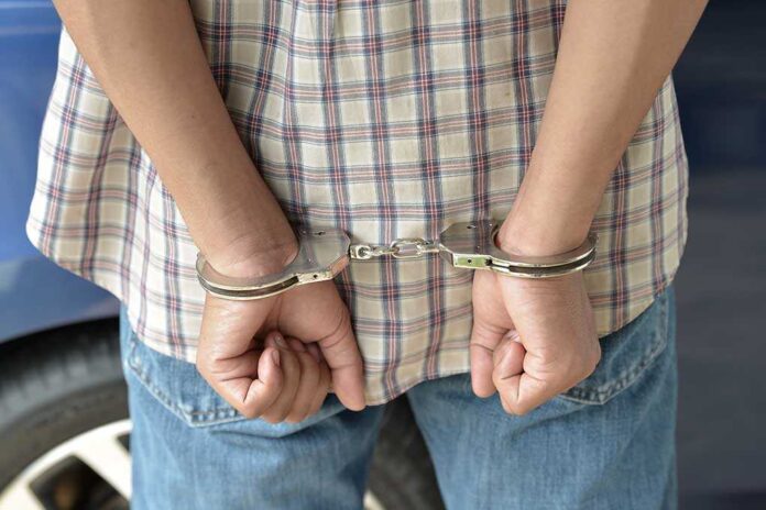A person in handcuffs viewed from behind, wearing a plaid shirt and denim jeans