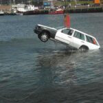 A white car being lifted out of the water by a crane at a port