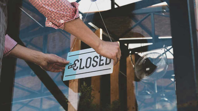 1162554778 Hand placing closed sign on glass door
