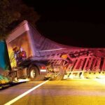 An overturned truck on the side of the road at night with emergency lights