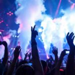 Crowd at a concert with hands raised and smoke effects in the background