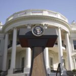 Press podium with presidential seal in front of the White House