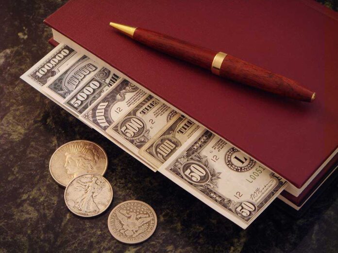 A stack of cash and coins on a book with a pen
