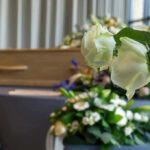 Fashion ICON DEAD – Entire Empire CRUMBLES White roses in front of a casket.
