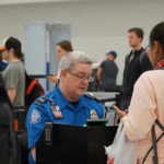 TSA Rolls Out NEW Program – Horrendous Fees! TSA agent checks passengers documents at airport security.