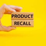 Hand holding Product Recall blocks on yellow background.