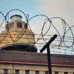 Barbed wire in front of a prison tower.