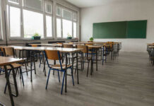 Empty classroom with desks, chairs, windows, and chalkboard.