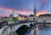 Scenic view of Zurich with a bridge, historic buildings, and a sunset sky