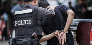 Police officer arrests handcuffed person.