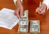Hands counting cash and reviewing financial documents on a wooden table