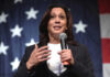 Socialist Insurgency Threatens Harris 2028 Woman speaking with microphone, American flag background.