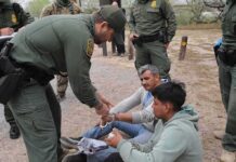 ICE Agents Tease Starving Kids Inside Facility law enforcement officer handcuffing two seated men outdoors