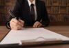Person in suit signing a document on a clipboard