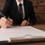 Person in suit signing a document on a clipboard