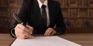 Person in suit signing a document on a clipboard