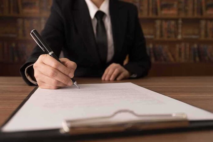 Person in suit signing a document on a clipboard