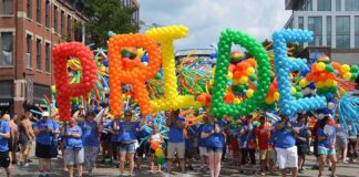 Dontrelle Inman at a Pride parade holding balloon letters spelling PRIDE