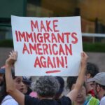 Teddy Williams at a protest holding a sign reading 'Make Immigrants American Again'
