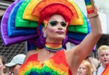 Dem Candidate’s Drag Queen OBSESSION Gets Weirder Drag performer in vibrant rainbow costume at a parade