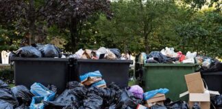 Overflowing dumpsters with piles of trash bags and cardboard