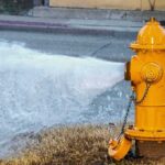 Yellow fire hydrant gushing water onto a street