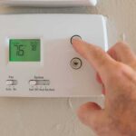 Commie Mamdani DEMANDS Residents To Do THIS Inside Their Homes Hand adjusting a digital thermostat on a wall
