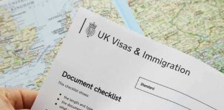 Hand holding UK visa and immigration document checklist over a map