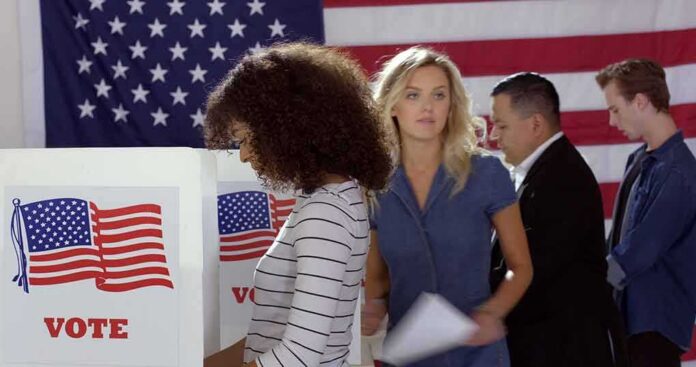 shutterstock_1739643257-1 Voters at polling booths in front of an American flag