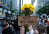 Protester holding flowers and a cardboard sign in a city street