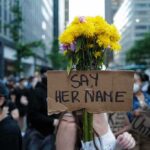 Protester holding flowers and a cardboard sign in a city street