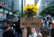 Protester holding flowers and a cardboard sign in a city street