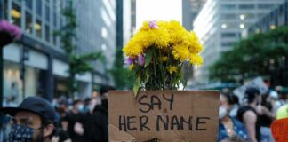 Protester holding flowers and a cardboard sign in a city street