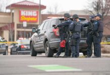 Five ARRESTED Over U.S Air Force Terror Plot! Police officers gather beside a patrol SUV at a taped-off scene