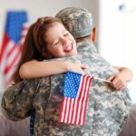 Child hugging a person in military uniform while holding a small U.S. flag