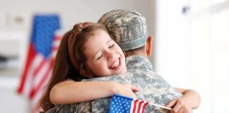 Child hugging a person in military uniform while holding a small U.S. flag