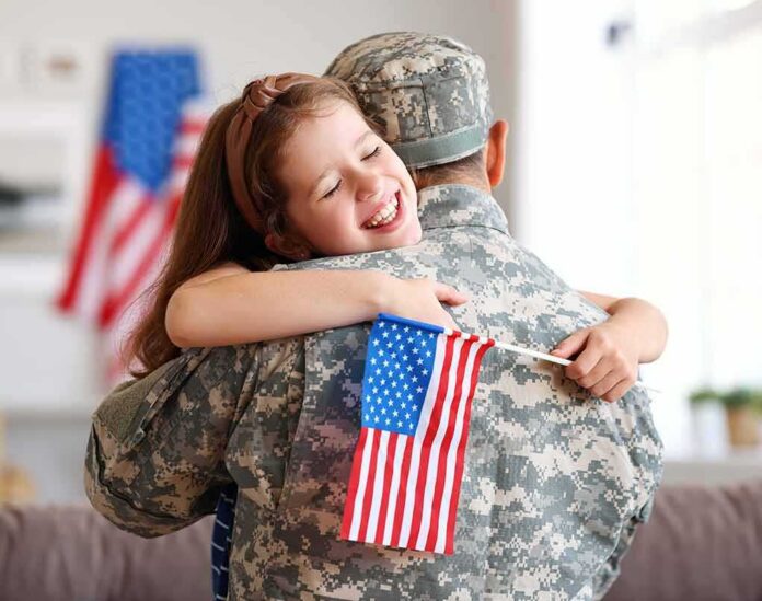Child hugging a person in military uniform while holding a small U.S. flag