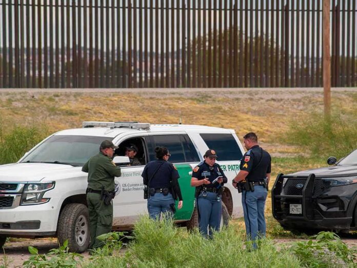 shutterstock_2015745392-1 law enforcement officers confer beside patrol vehicles near a border fence