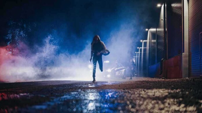 Person running at night near police car with flashing lights