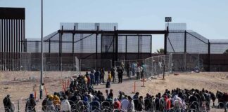 Crowd of people lining up near a border fence with barbed wire