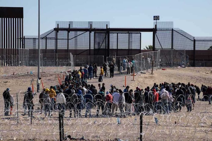 Crowd of people lining up near a border fence with barbed wire